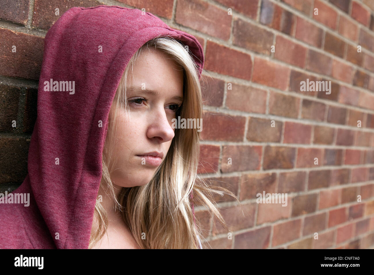Sulky blonde teenage girl wearing a hoodie leaning against a wall, Billericay Essex UK Stock Photo