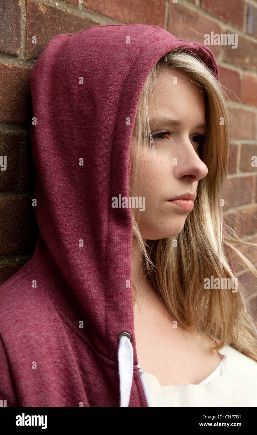 Blonde teenage girl wearing a hoodie leaning against a wall, Billericay Essex UK Stock Photo