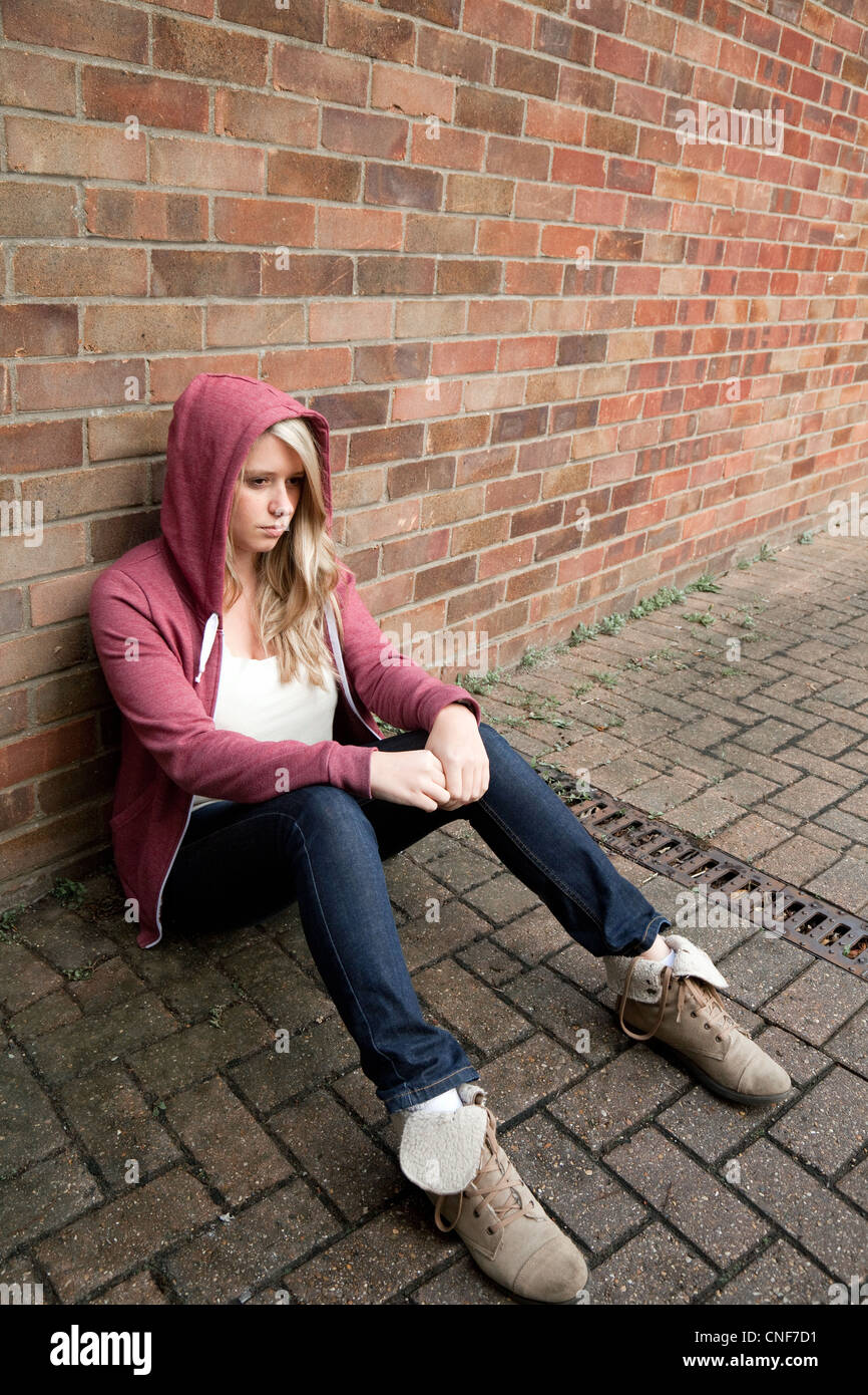 Blonde teenage girl wearing a hoodie sitting against a wall, Essex UK Stock Photo