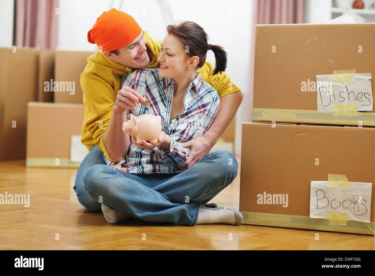 Young couple among boxes putting coin in piggy bank Stock Photo - Alamy