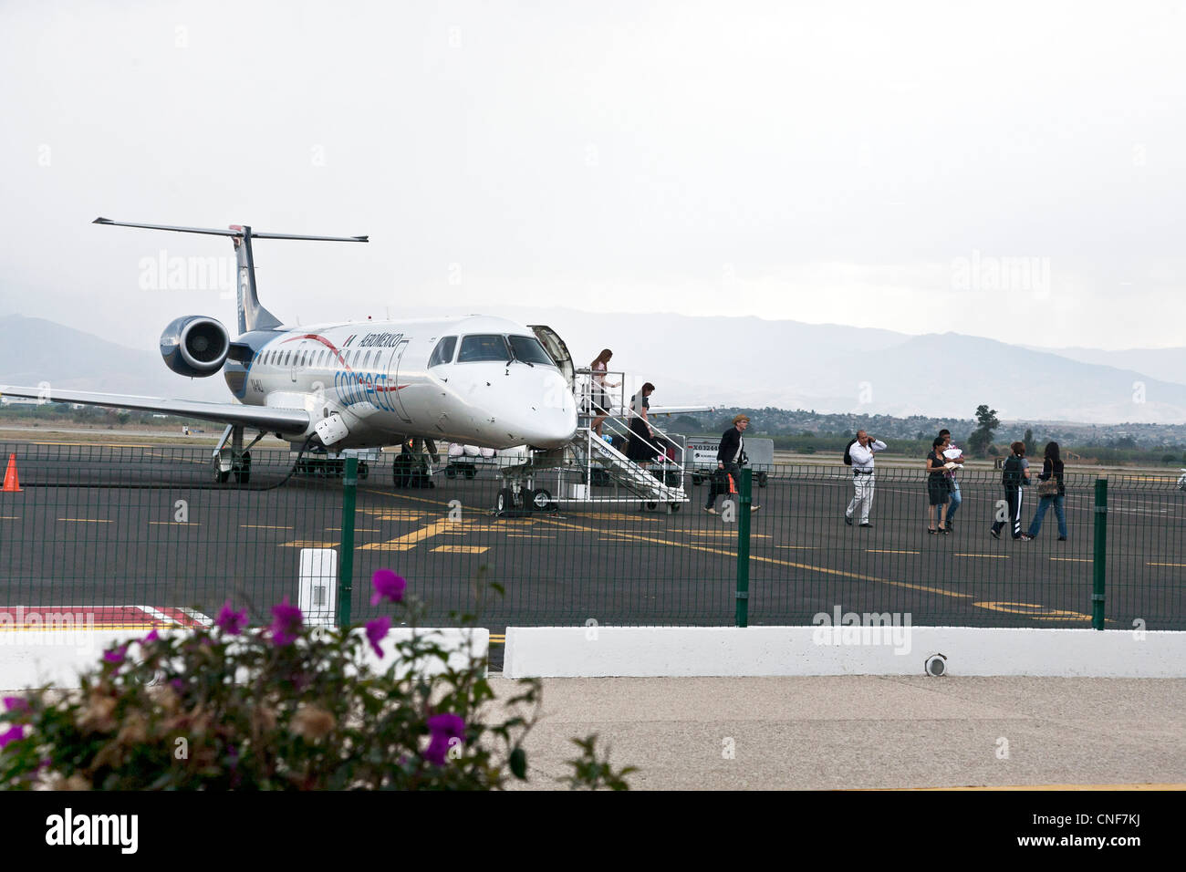 passengers disembark from Aeromexico commuter jet on foot across tarmac against backdrop of mountains at Oaxaca Airport Mexico Stock Photo
