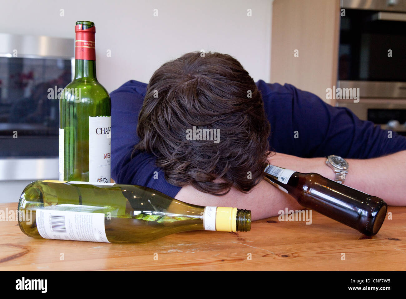 Drunk young man with hangover and empty bottles of wine and beer,  UK - Posed by a Model Stock Photo
