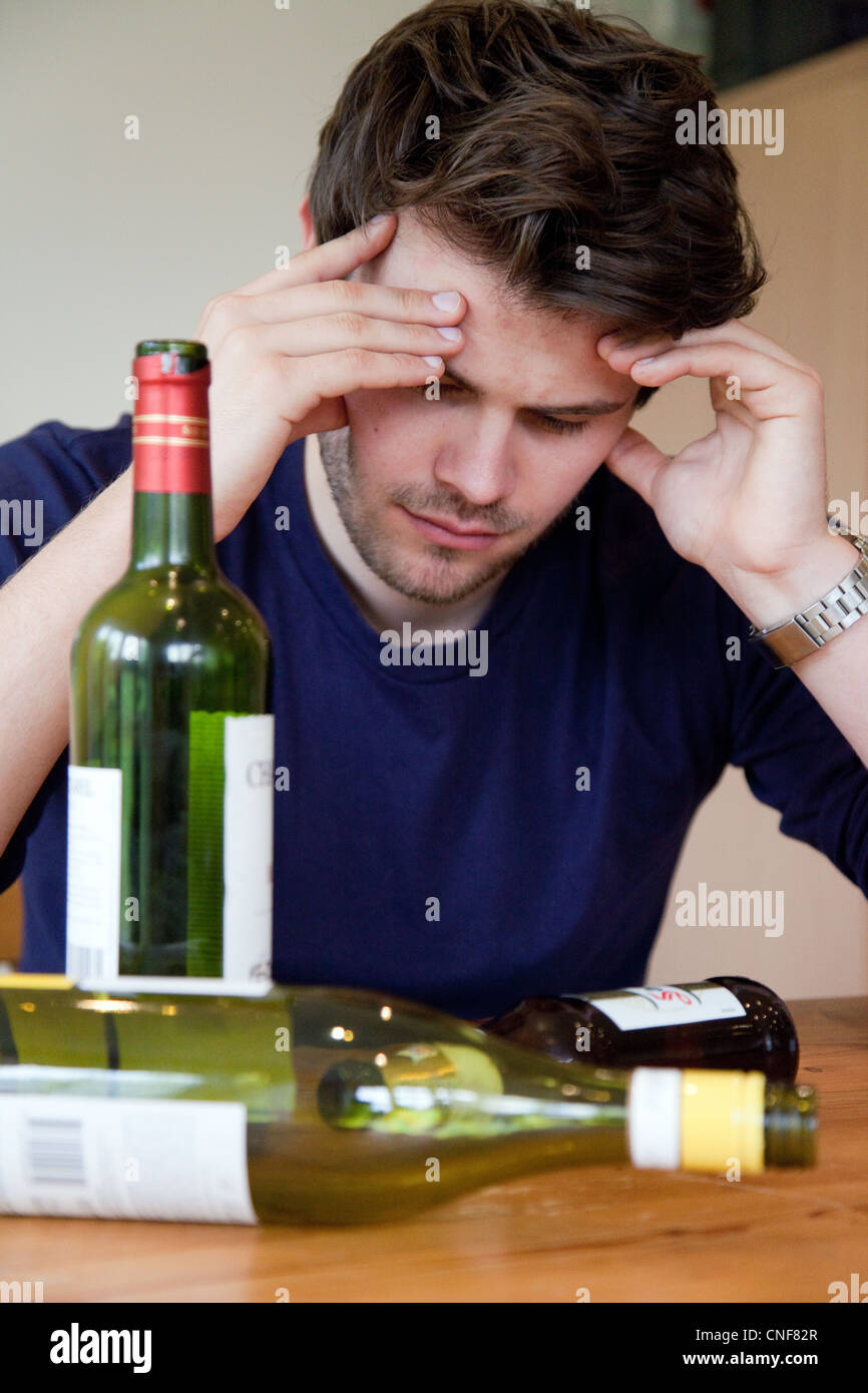 Drunk young man with hangover and empty bottles of wine and beer, UK