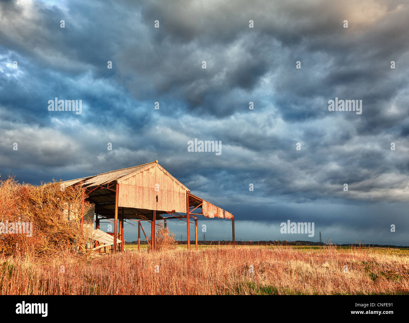 Storm clouds over sunlit deserted and ruined barn on farmland Stock Photo