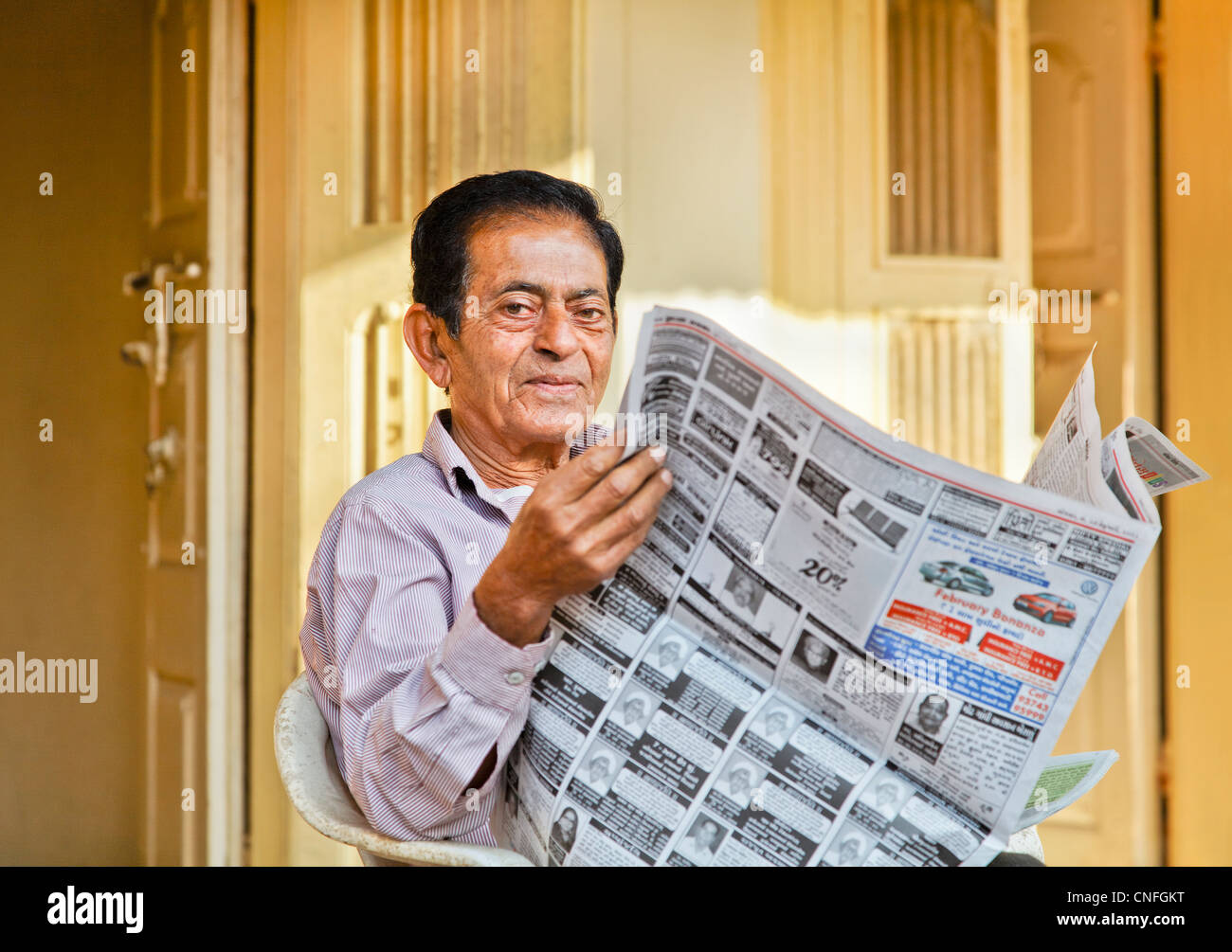 Senior Indian gentleman portrait outside his hinterland village home reading local language morning newspaper on front patio Stock Photo