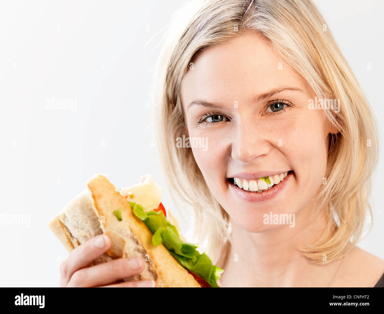 Woman smiling with lettuce caught in teeth, studio shot Stock Photo