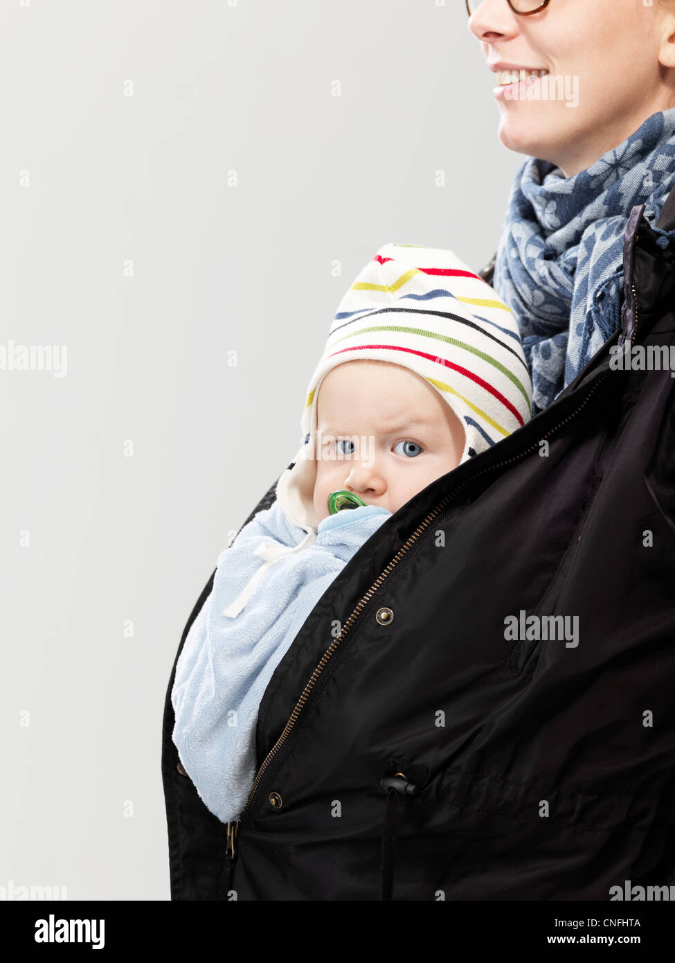Portrait of baby tucked into mother's jacket, studio shot Stock Photo