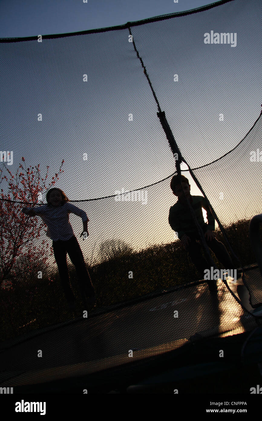 children jumping on trampoline late in afternoon with dramtic late afternoon weather and atmosphere Stock Photo
