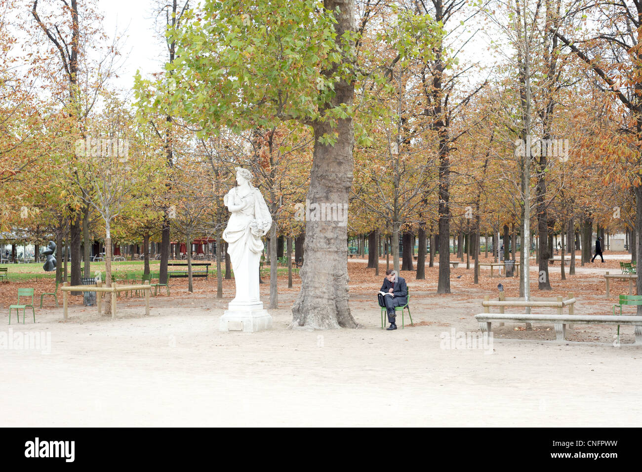 A man sitting in a chair reading, next to a statue in the Tuileries Garden in Paris, France. Stock Photo