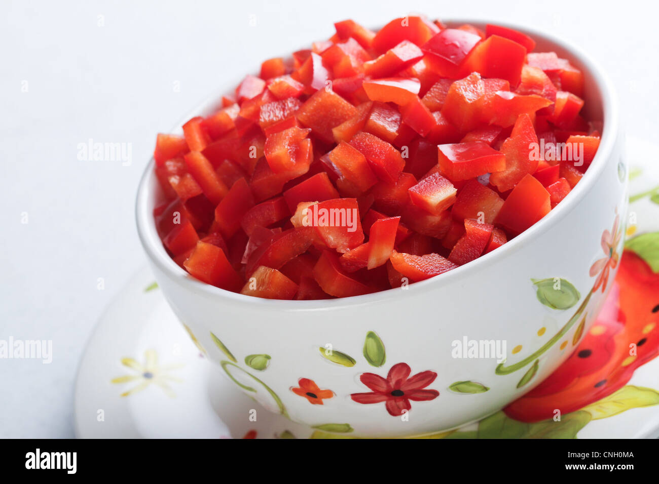 A macro image of a decorative bowl full of chopped, colorful red pepper on a matching plate with a white background. Stock Photo