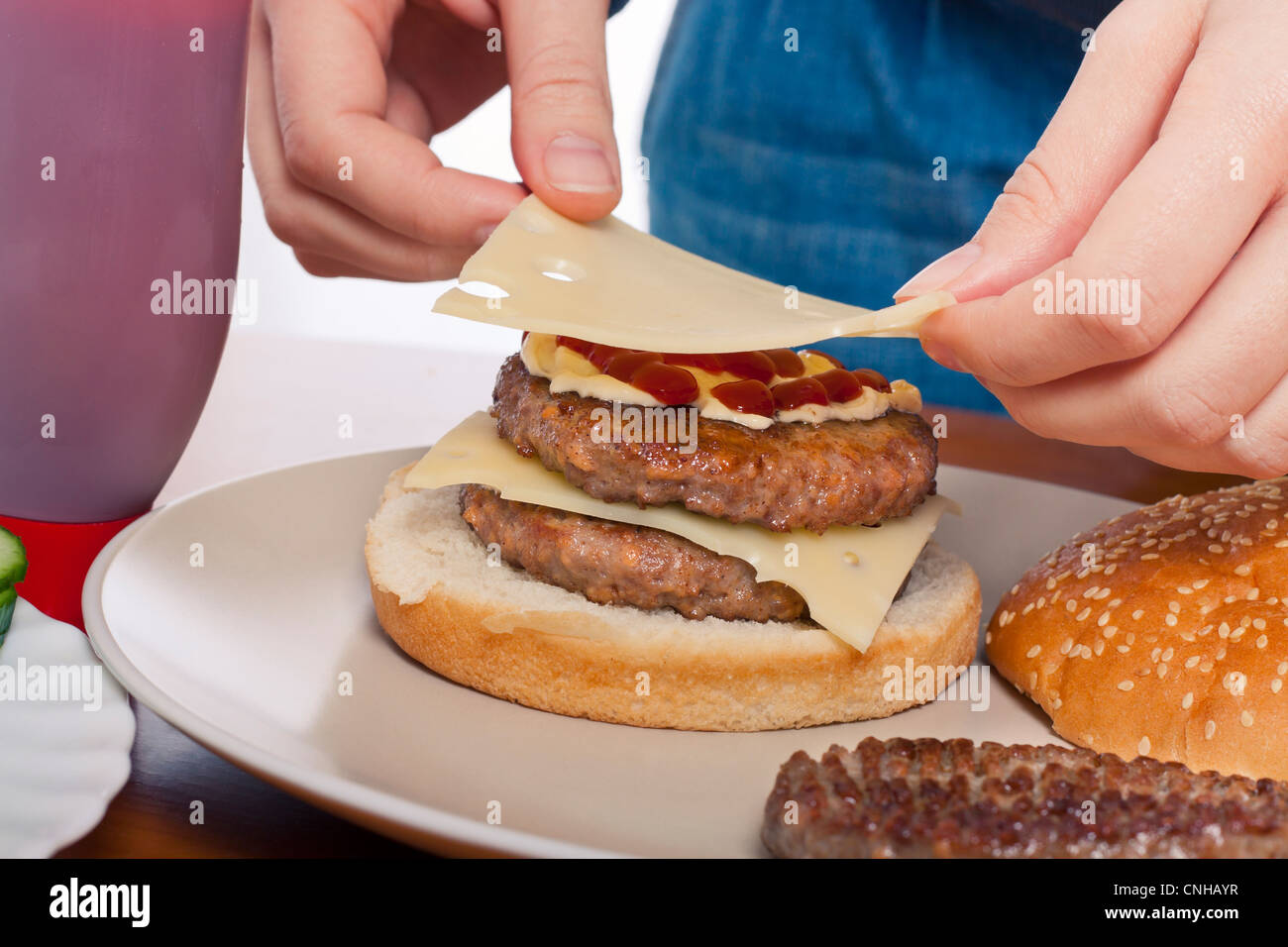 Close up of hands putting cheese on homemade double hamburger Stock