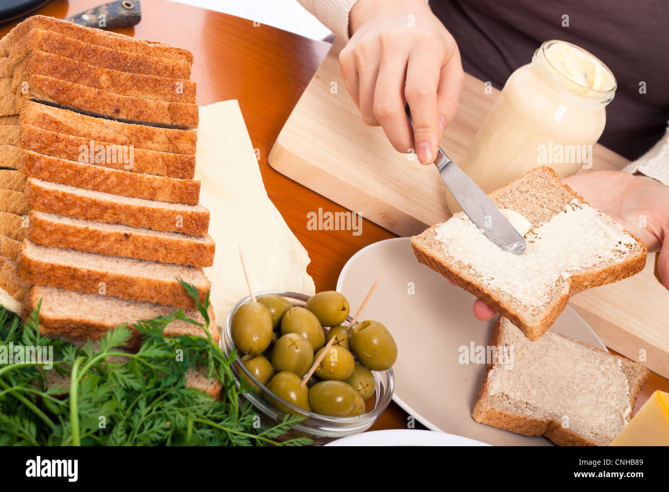 Detail of kitchen table and female hands spreading mayonnaise preparing sandwich. Stock Photo