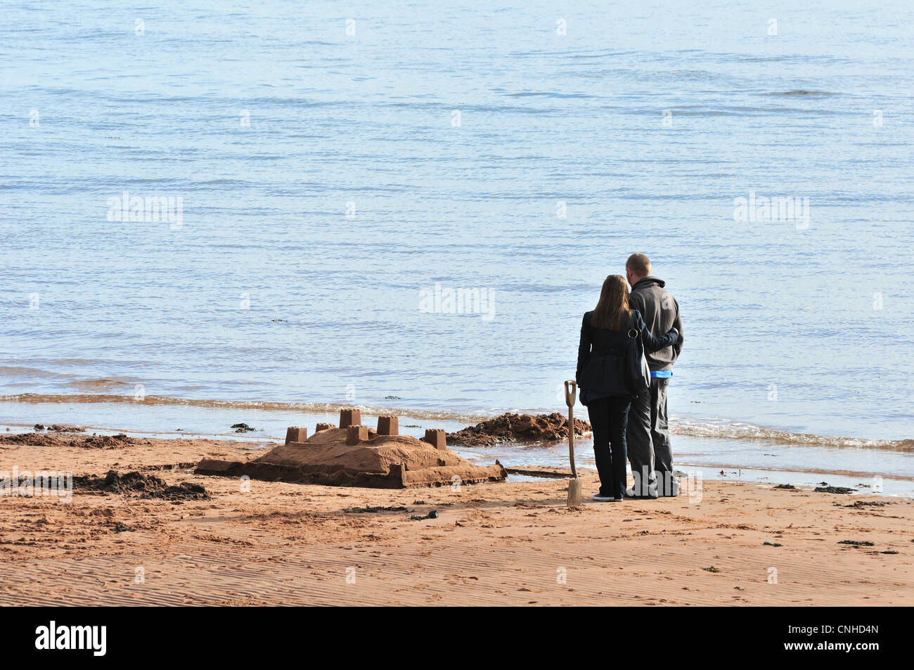 Concept. Young man and woman stand beside a sandcastle built on beach and contemplate the future together. Stock Photo