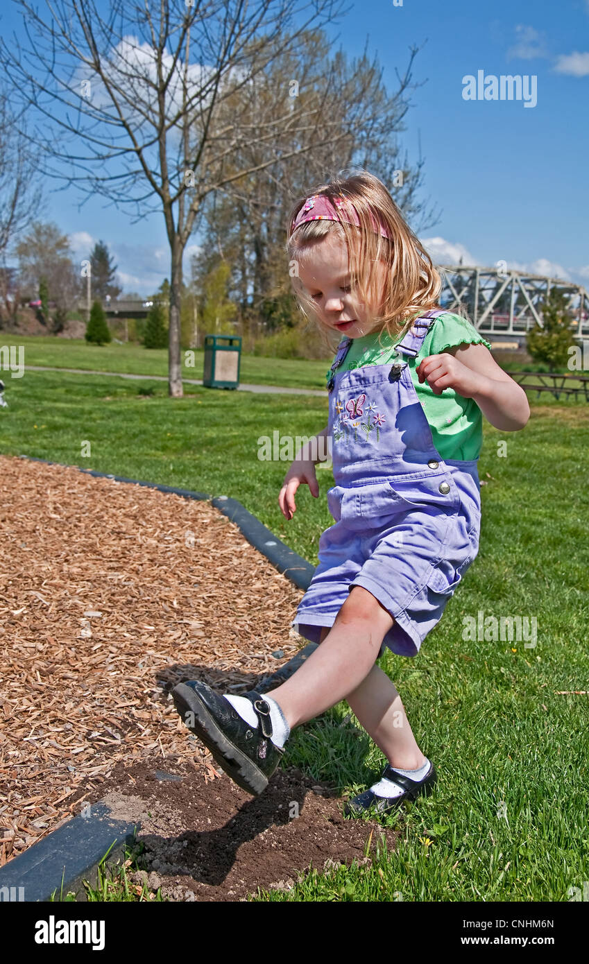 This Caucasian 3 year old toddler girl is stomping dirt in her black Mary Jane shoes outdoors in a park. Stock Photo