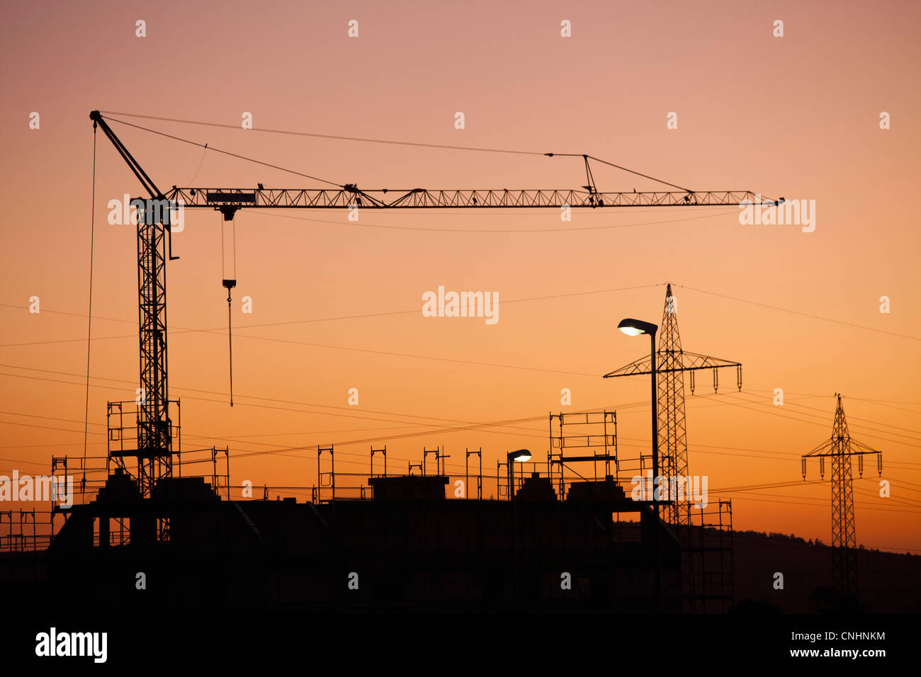 A construction crane and electricity pylons silhouetted against a sunset sky Stock Photo