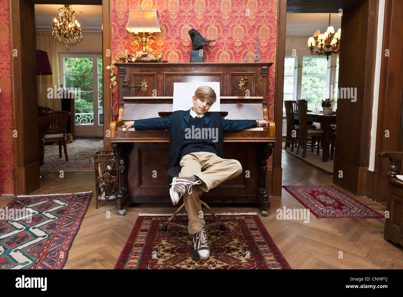 A boy with a cool attitude posing at an old-fashioned upright piano Stock Photo