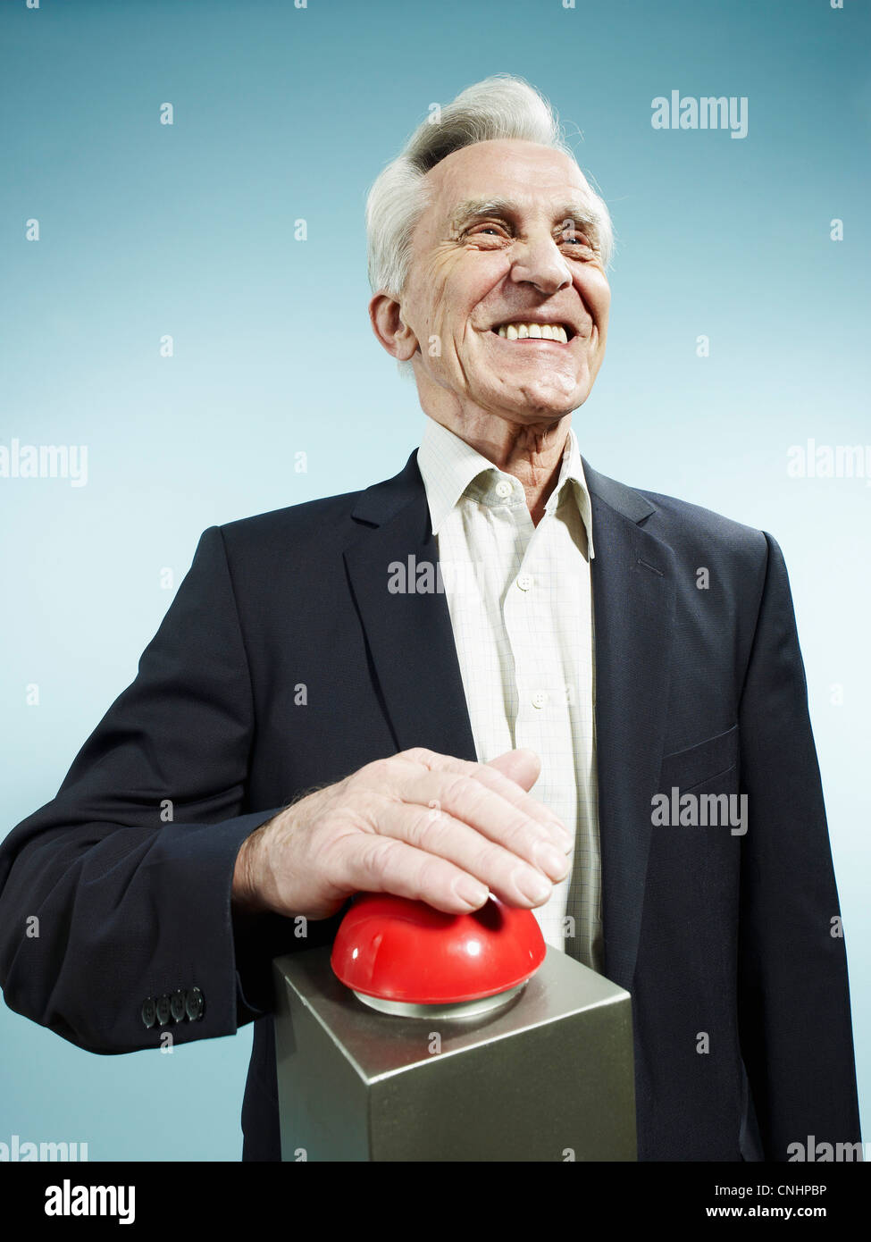 A grinning senior man pushing a red game show buzzer Stock Photo