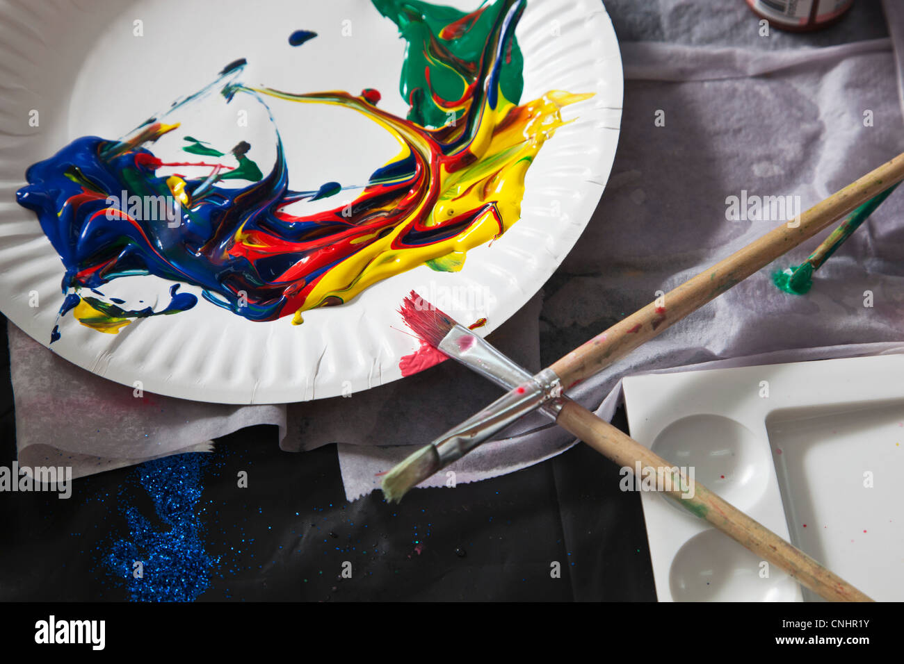 Heaps of acrylic paint on a paper plate and paintbrushes Stock Photo