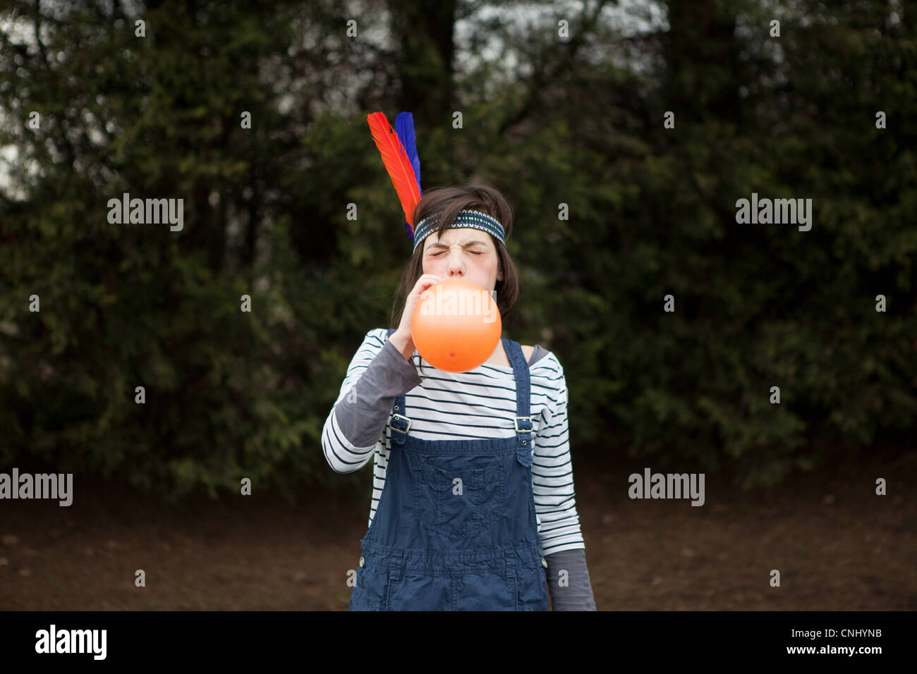 Young woman in headdress, blowing up a balloon Stock Photo