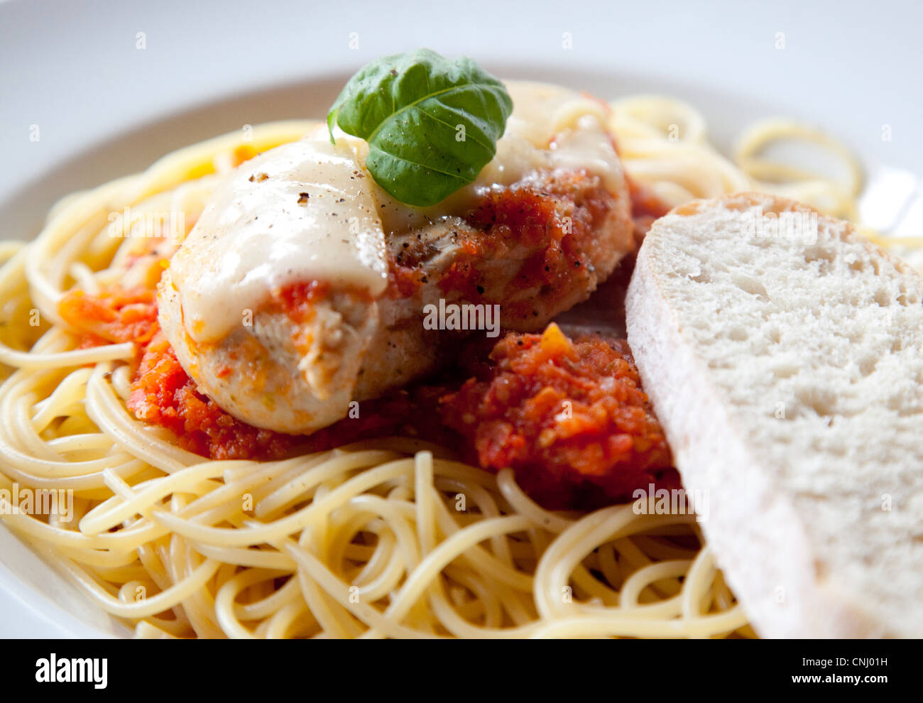A tasty colour photo of Chicken Parmesan alongside a slice of white bread. Stock Photo
