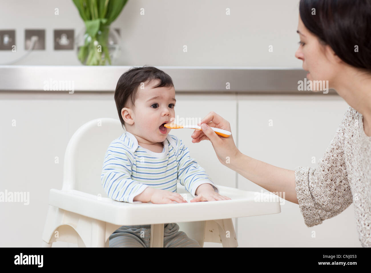 Mother feeding baby son in high chair Stock Photo Alamy