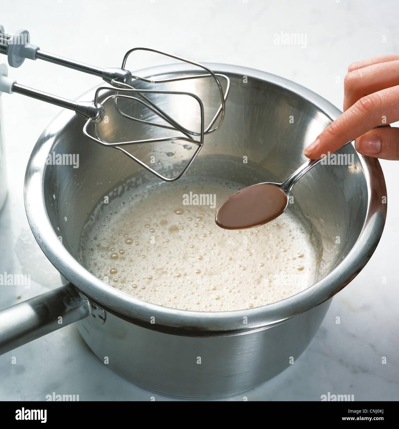 Adding melted nougat to the beaten egg and sugar mixture Stock Photo