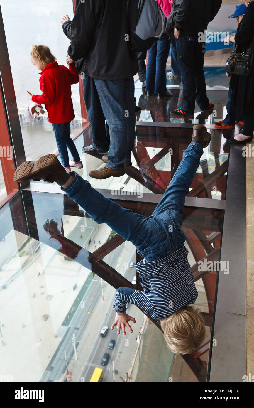 A child finds a way to get a different view from the Blackpool Tower Eye 'Skywalk' by standing on his head. Stock Photo