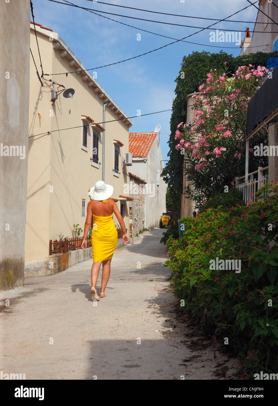 Female dressing yellow walking on street of small town Unije on Unije island in Croatia. Stock Photo