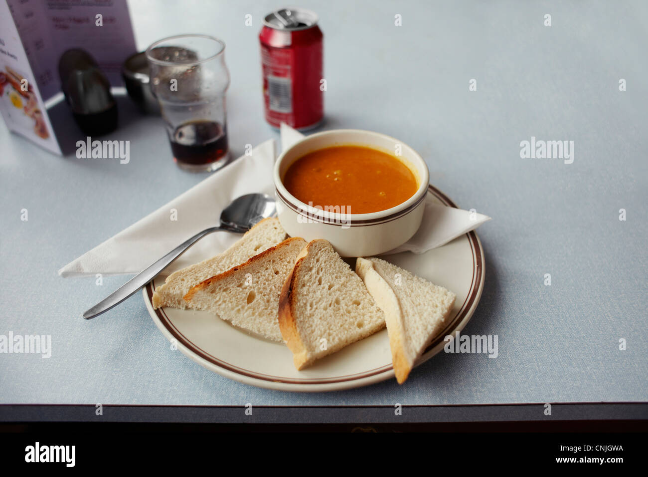 A bowl of soup with sliced bread and a cola drink in a cafe on table Stock Photo