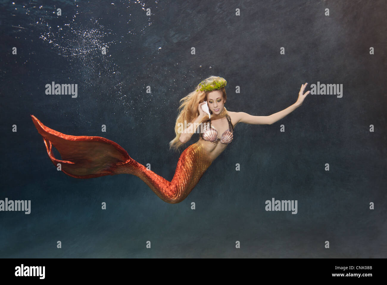 Young mermaid swimming underwater while talking on her shellphone Stock Photo