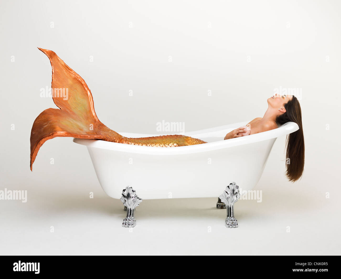 Mermaid bathing herself in her Victoria + Albert claw foot bathtub Stock Photo