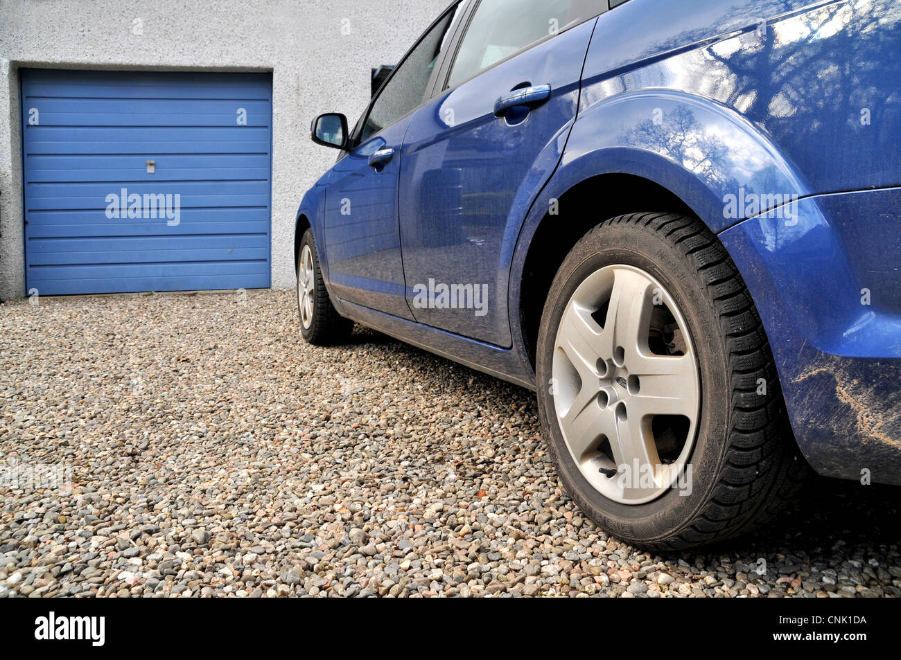 A blue car parked in front of a closed garage door in the driveway of a house. Stock Photo