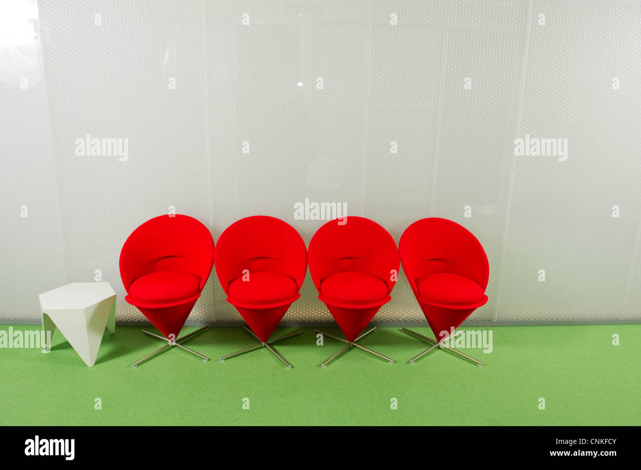 Four red chairs and a white table on a green carpet Stock Photo