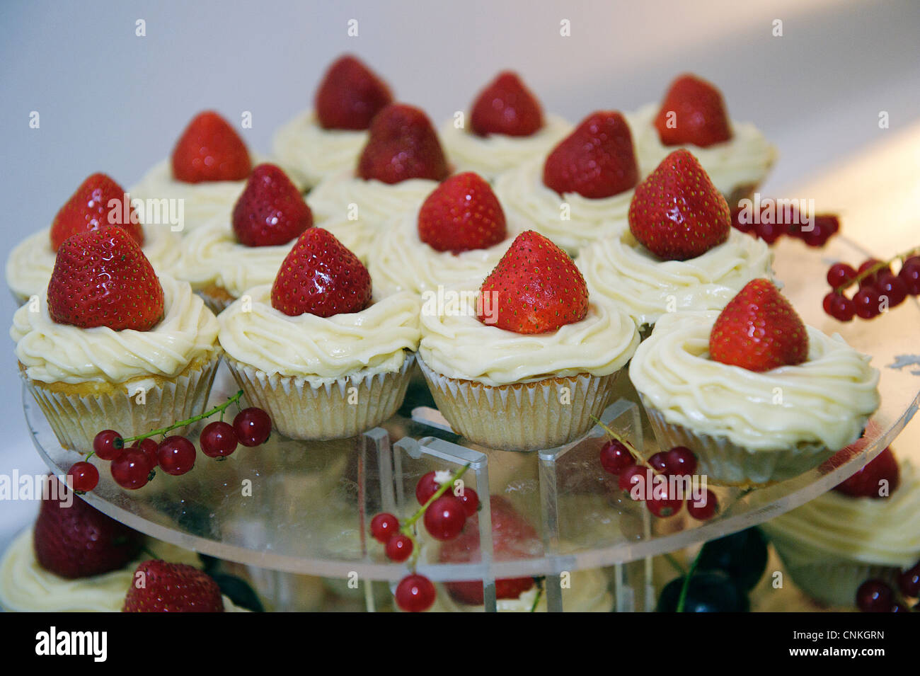 cake stand with fresh strawberry cupcakes and cream or butter icing with redcurrants Stock Photo