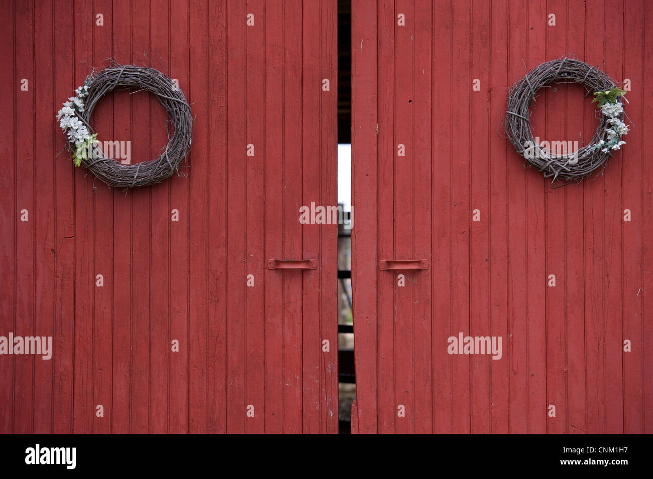 Grapevine wreath decorations hanging on red barn doors entrance. Stock Photo