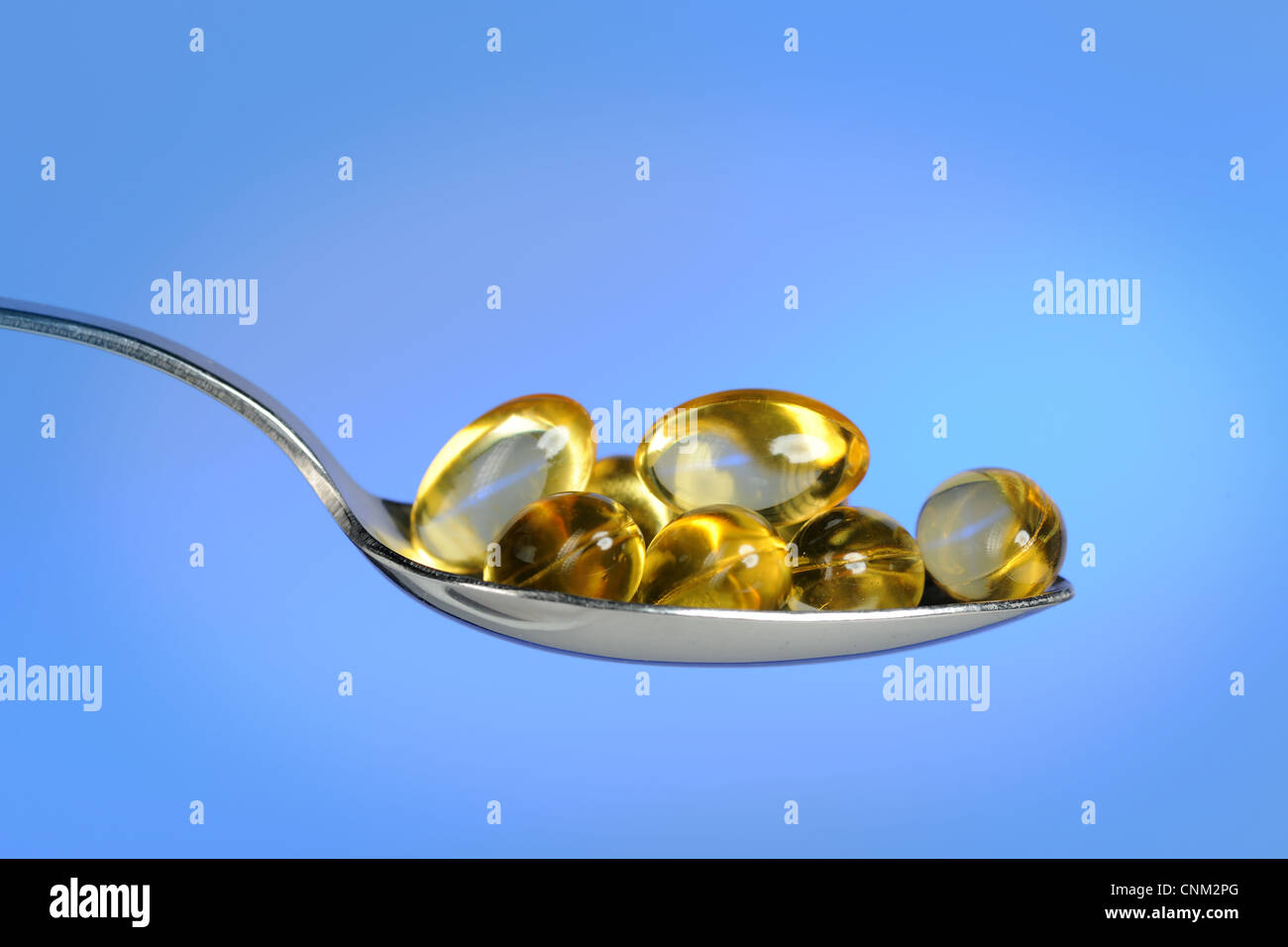 Spoon with fish oil pills over light blue background Stock Photo