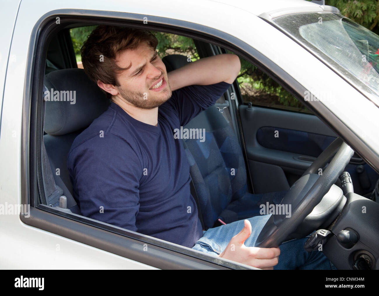 Young man driving a car with neck pain, UK Stock Photo