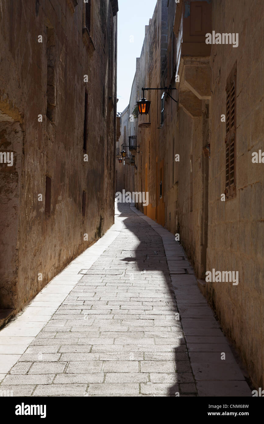 A typical narrow alleyway with sunlight catching the glass in a streetlight in Mdina Malta, Europe Stock Photo