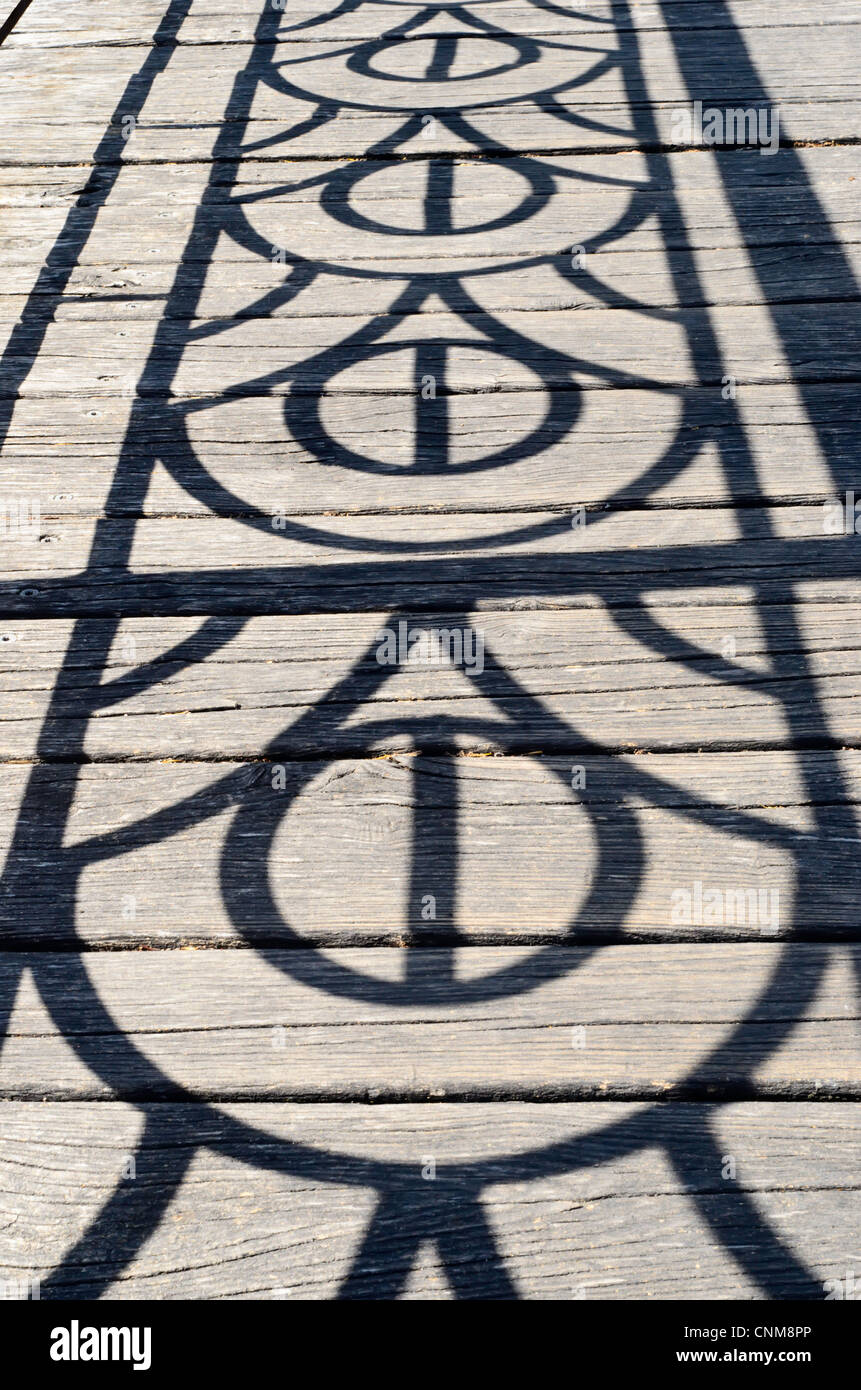 One pattern on another: Shadows of symmetrical iron railing on planks of wooden footbridge Stock Photo