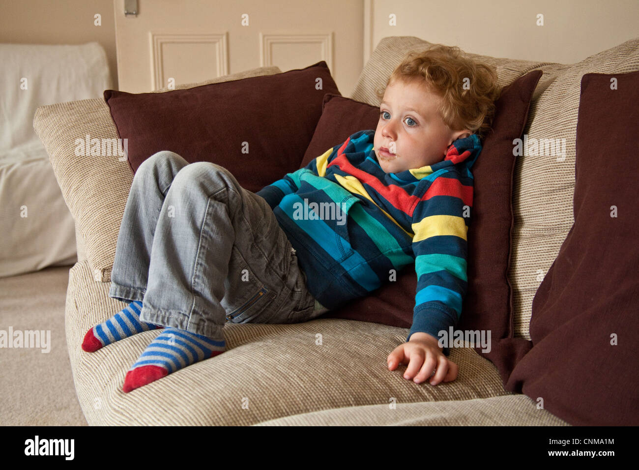 Three year old boy feeling ill or unwell sitting on a sofa, Hampshire, England, united Kingdom. Stock Photo
