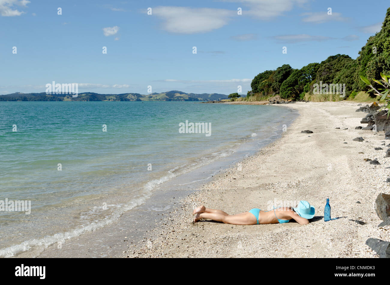 A woman sunbathing alone on an empty new Zealand beach. Stock Photo