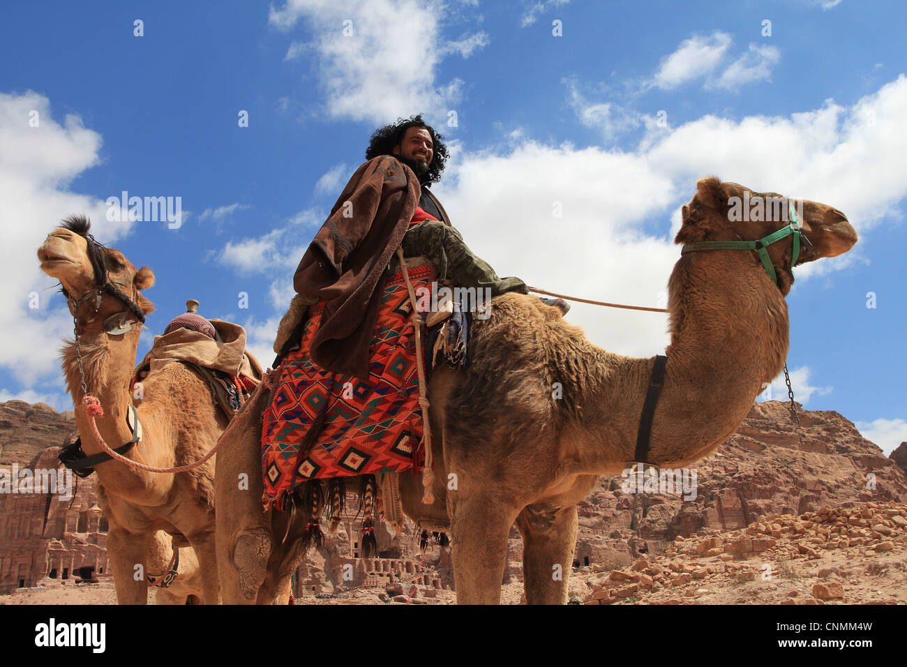 A Bedouin in front of the Royal tombs in Petra trying to hire tourists for a ride with his camels, Jordan. Stock Photo