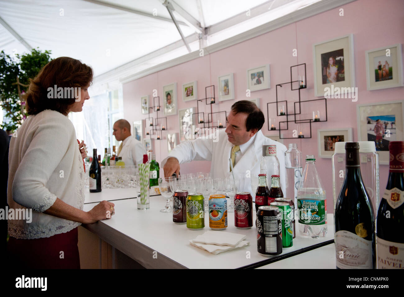 Older caucasian male bartender in white suit jacket serving drinks at a