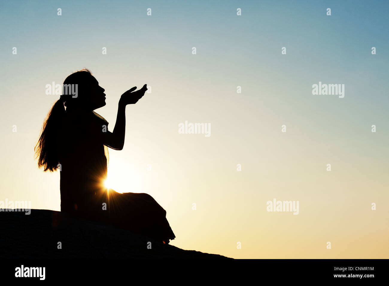 Indian girl sitting holding out her hands at sunset. Silhouette Stock Photo