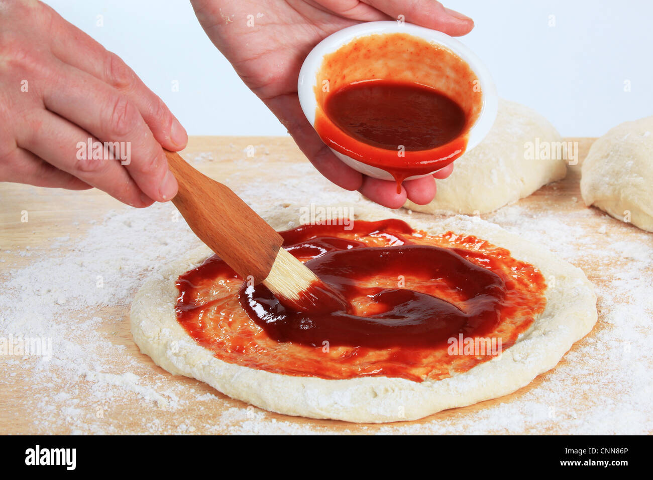 Cook spreading tomato sauce over pizza dough Stock Photo Alamy
