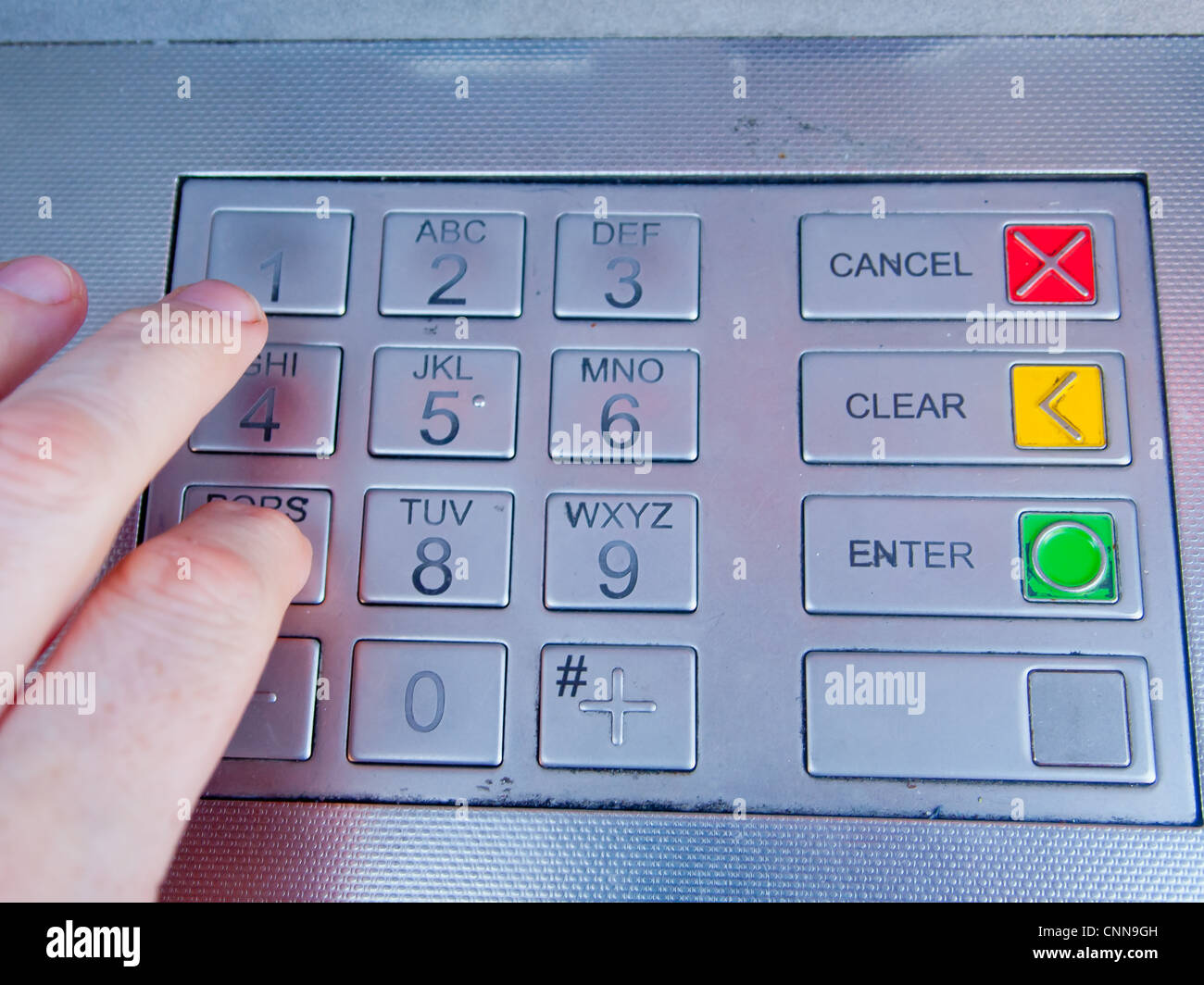 An ATM machine with worn numbers with a hand pressing the digits Stock Photo