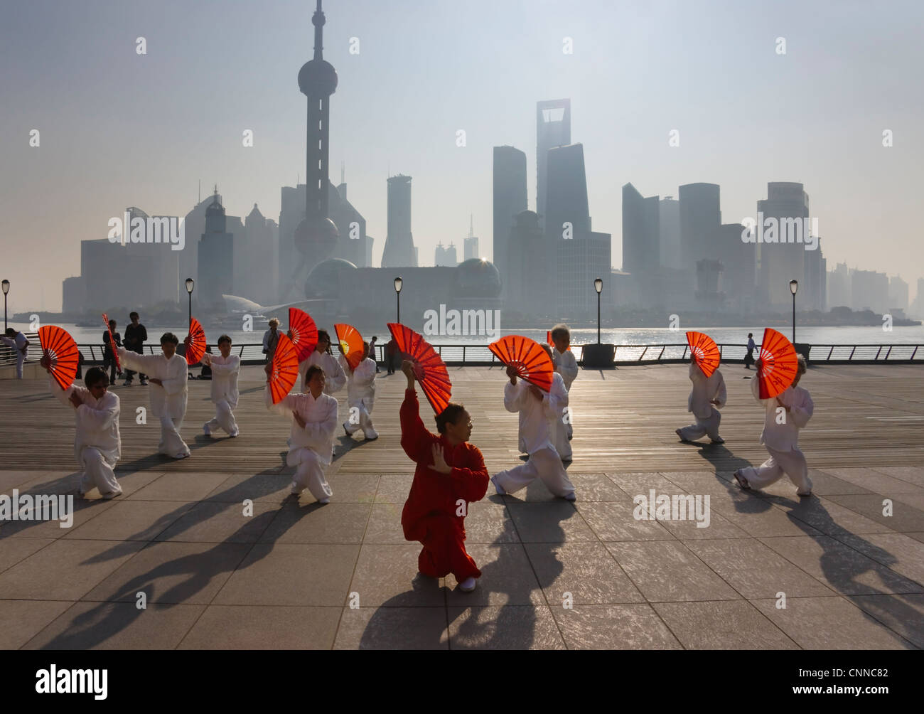 People practicing Taiji with red fans on the Bund, Pudong skyline in the distance, Shanghai, China Stock Photo