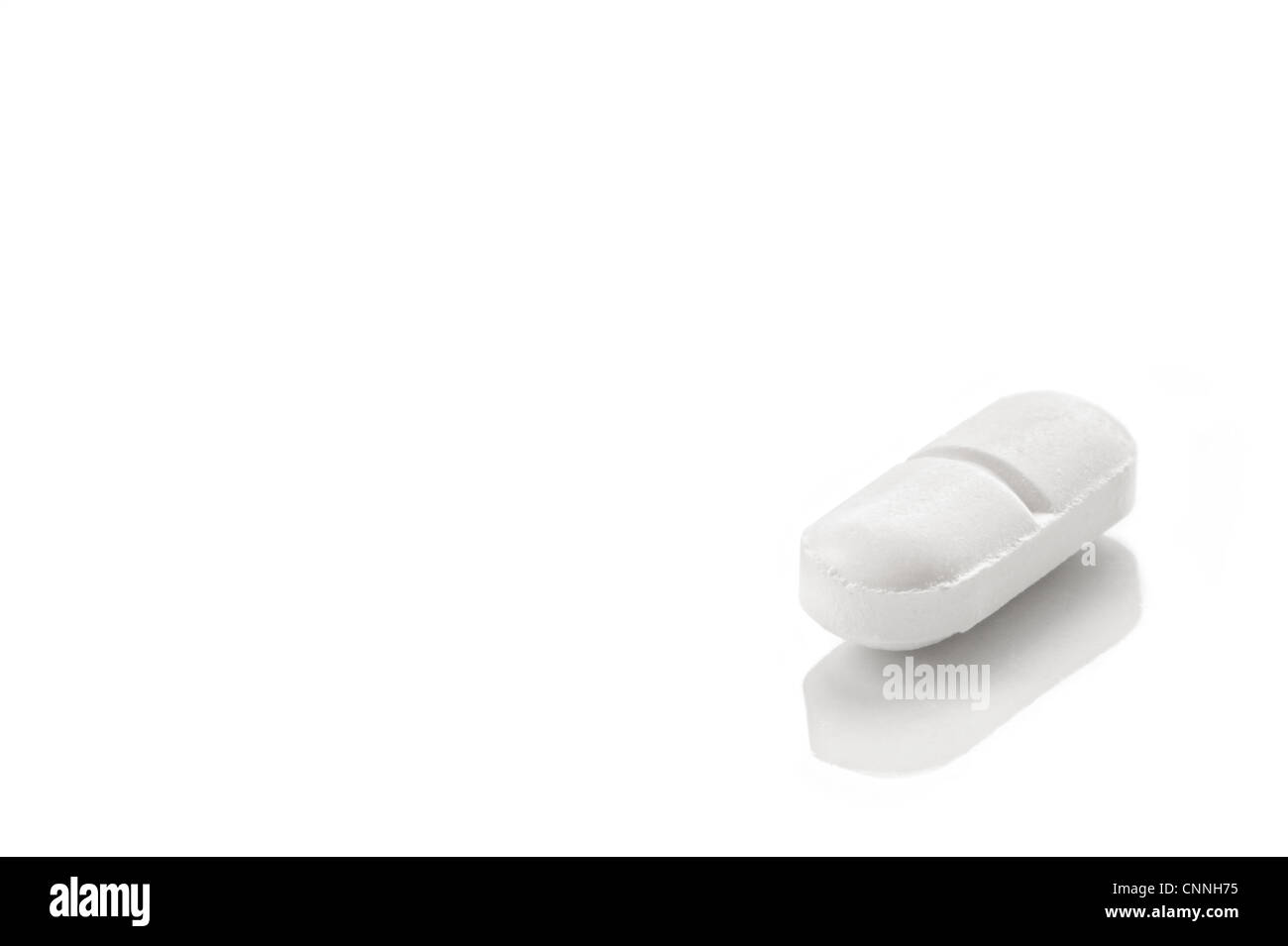 White lozenge shaped tablet on a white reflective surface Stock Photo