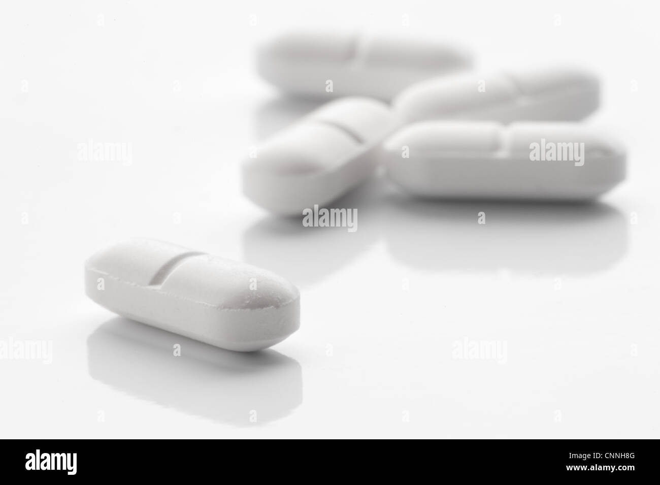 White lozenge shaped tablets on a white reflective surface Stock Photo