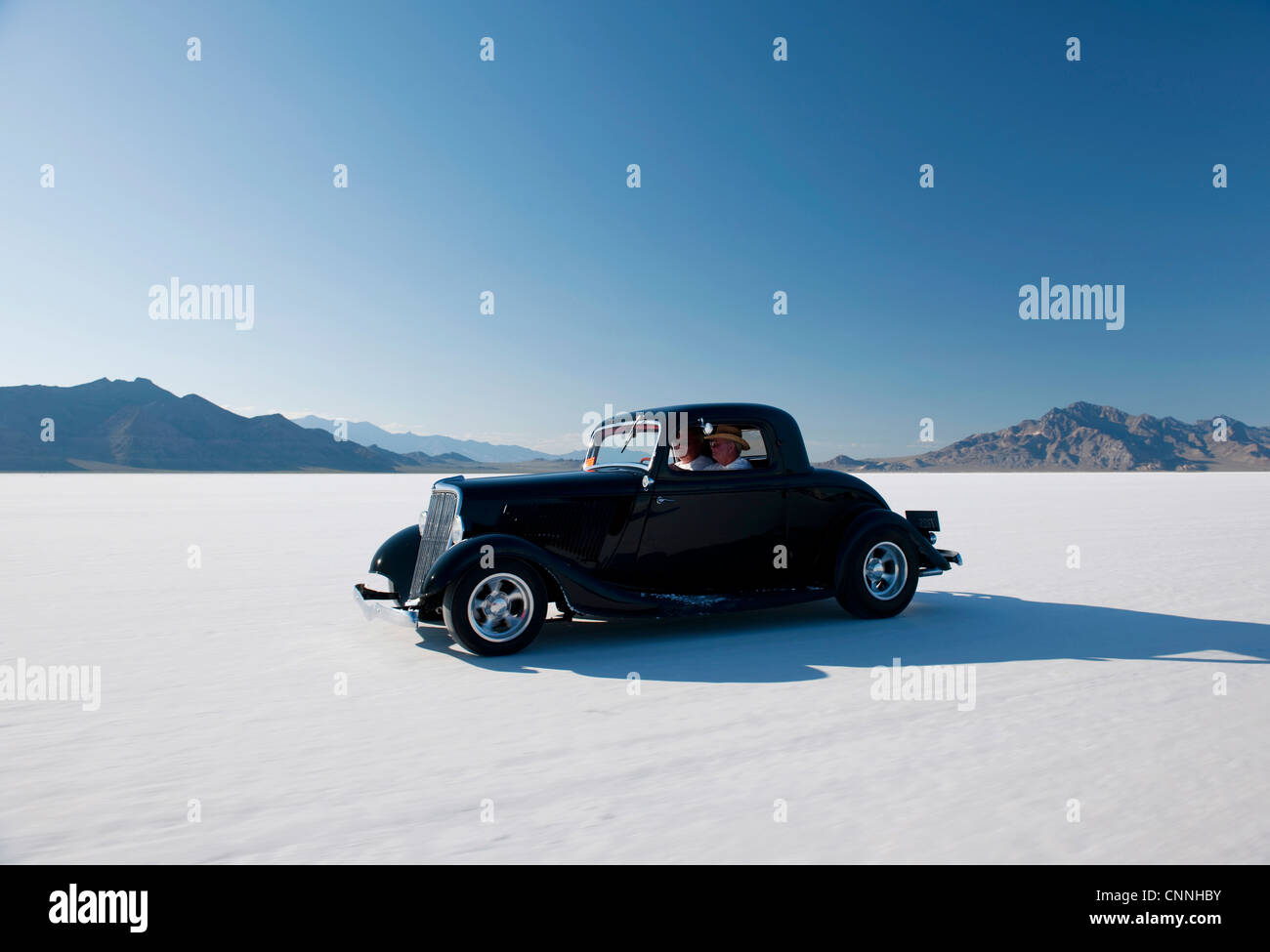 retro car driving across bonneville salt flats US blue sky white sand